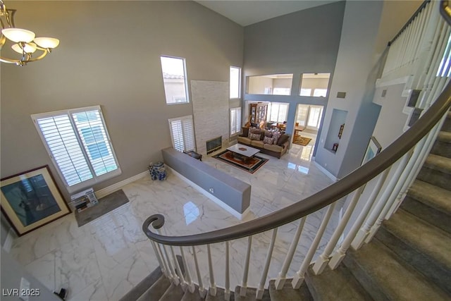 stairs featuring a towering ceiling, a stone fireplace, and a chandelier