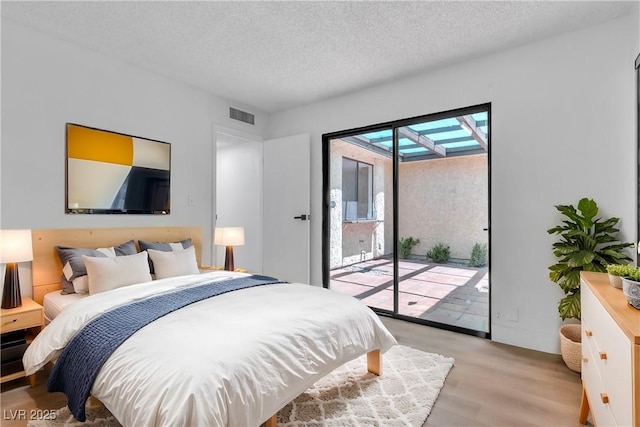 bedroom featuring access to exterior, light hardwood / wood-style flooring, and a textured ceiling