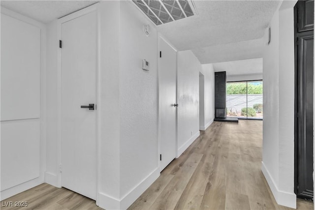 corridor with a textured ceiling and light wood-type flooring