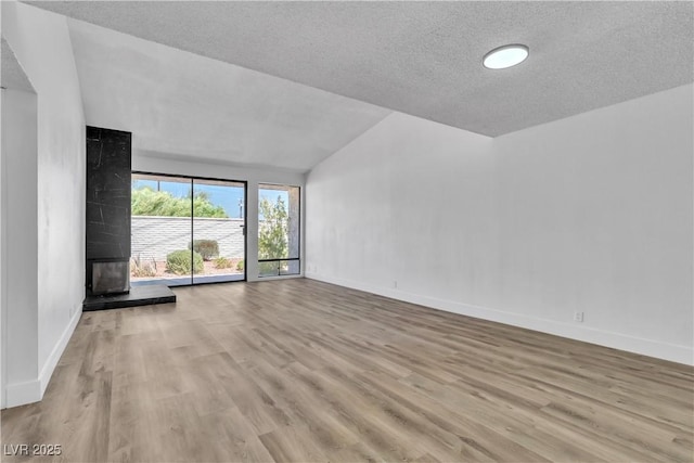 spare room featuring a textured ceiling, a multi sided fireplace, lofted ceiling, and light wood-type flooring