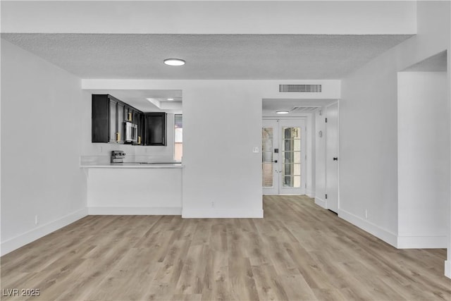 unfurnished living room featuring light hardwood / wood-style flooring, a textured ceiling, and french doors