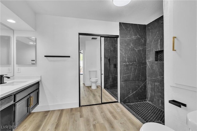 bathroom with tiled shower, wood-type flooring, vanity, and toilet