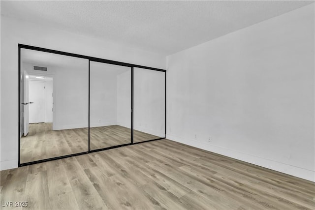 unfurnished bedroom with light wood-type flooring, a textured ceiling, and a closet