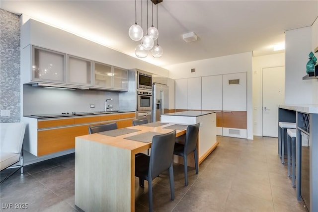 kitchen featuring sink, a breakfast bar area, appliances with stainless steel finishes, a kitchen island, and decorative light fixtures