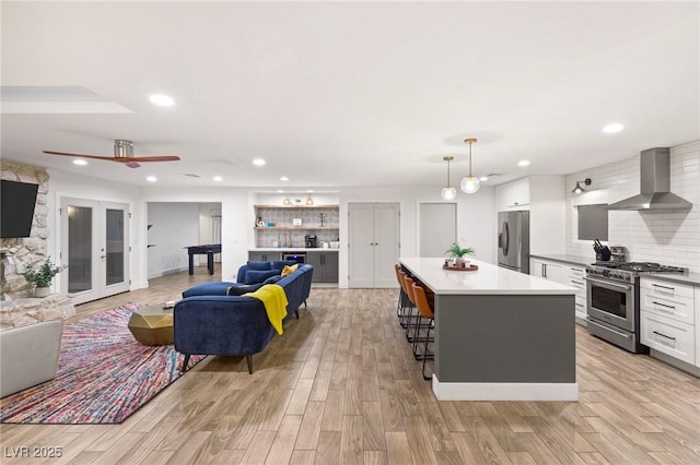 kitchen featuring backsplash, white cabinetry, wall chimney range hood, and appliances with stainless steel finishes