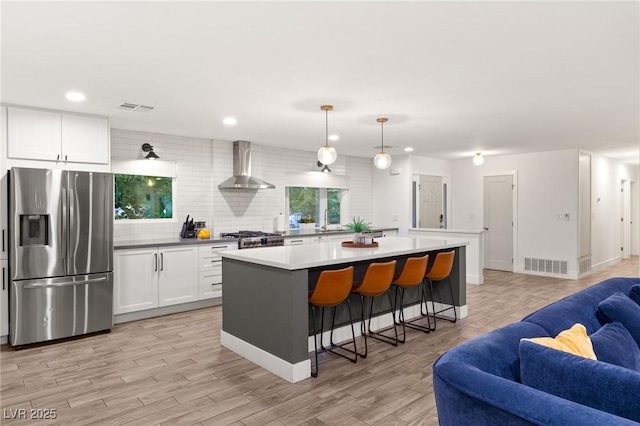 kitchen with a center island, wall chimney exhaust hood, stainless steel fridge with ice dispenser, decorative light fixtures, and white cabinets