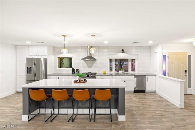 kitchen with white cabinetry, wall chimney exhaust hood, hanging light fixtures, decorative backsplash, and appliances with stainless steel finishes