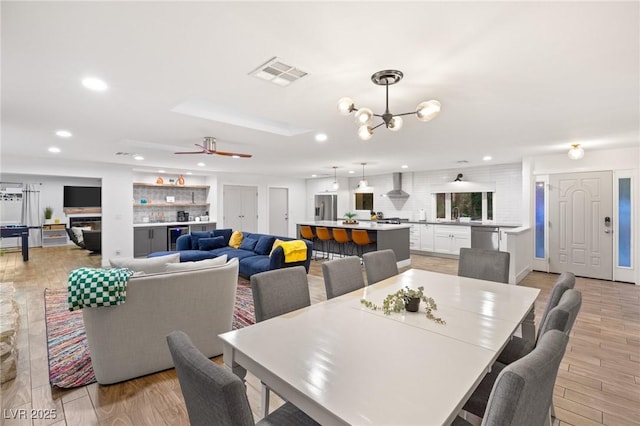 dining room with ceiling fan with notable chandelier, light hardwood / wood-style floors, and wine cooler