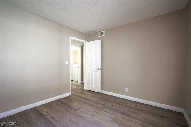 empty room with hardwood / wood-style floors, a textured ceiling, and washer / clothes dryer