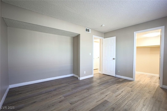 unfurnished bedroom with a textured ceiling, hardwood / wood-style flooring, a spacious closet, and a closet