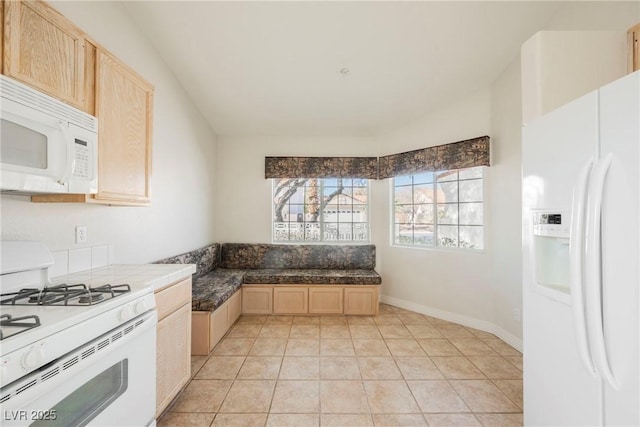 kitchen with light tile patterned floors, light brown cabinetry, and white appliances