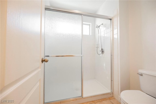 bathroom featuring toilet, a shower with shower door, and tile patterned flooring