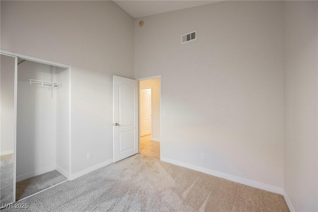 unfurnished bedroom featuring light colored carpet, high vaulted ceiling, and a closet