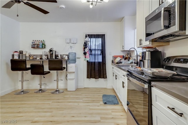 kitchen featuring ceiling fan, sink, stainless steel appliances, white cabinets, and light wood-type flooring