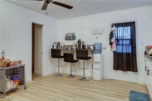 bar with white cabinets, light hardwood / wood-style floors, and ceiling fan