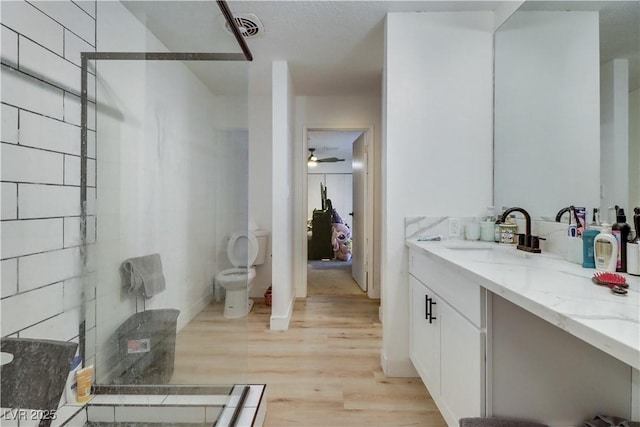 bathroom with walk in shower, vanity, ceiling fan, wood-type flooring, and toilet