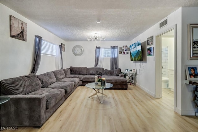 living room with a notable chandelier, light wood-type flooring, and a textured ceiling