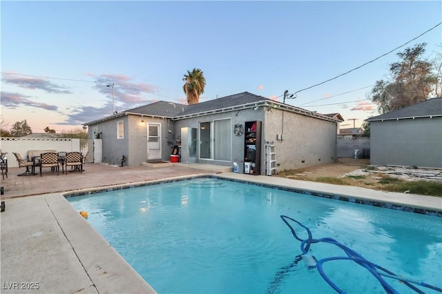 back house at dusk featuring a fenced in pool and a patio