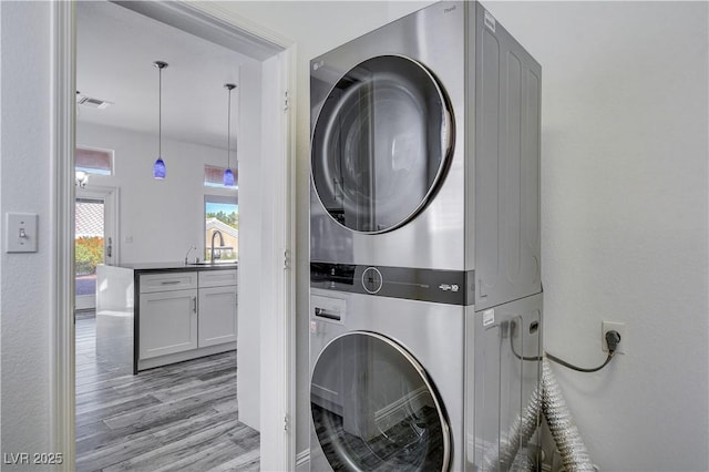 laundry room with light hardwood / wood-style floors, stacked washing maching and dryer, and sink