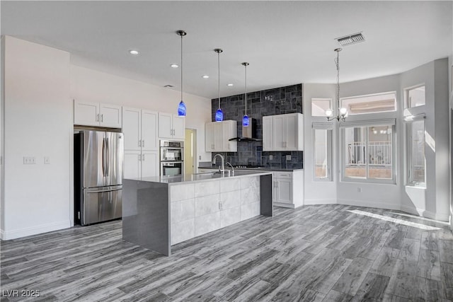 kitchen with white cabinetry, a center island with sink, wall chimney exhaust hood, and appliances with stainless steel finishes