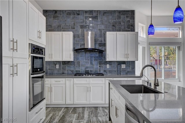 kitchen featuring white cabinets, sink, wall chimney exhaust hood, and pendant lighting