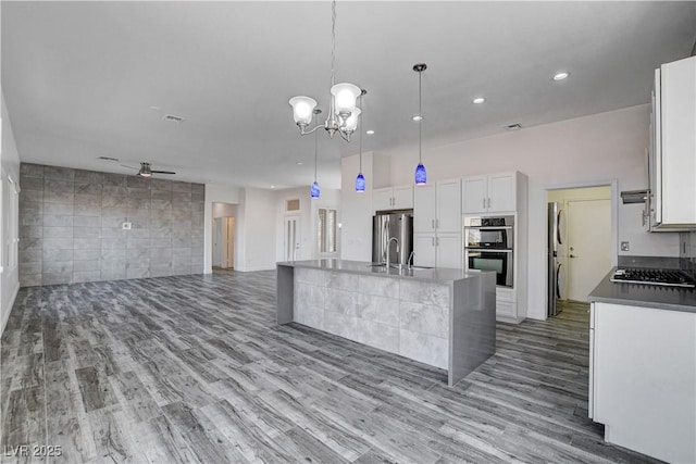 kitchen featuring appliances with stainless steel finishes, ceiling fan with notable chandelier, a kitchen island with sink, pendant lighting, and white cabinets