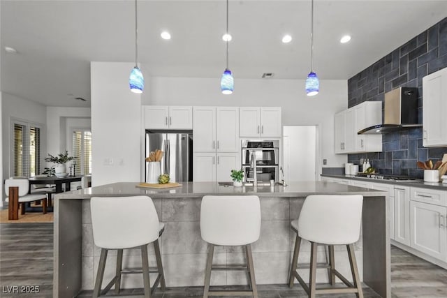 10300 Bent Brook Pl, Las Vegas, NV 89134 - kitchen with a kitchen island with sink, appliances with stainless steel finishes, wood finished floors, a breakfast bar, and wall chimney exhaust hood