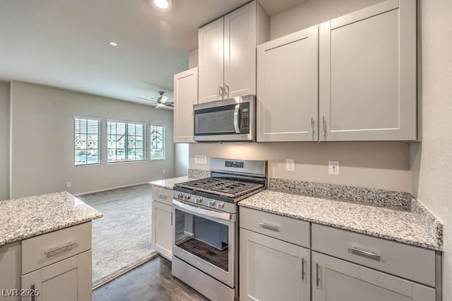 kitchen featuring white cabinetry, ceiling fan, light stone counters, dark carpet, and appliances with stainless steel finishes