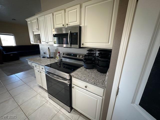 kitchen with light tile patterned flooring, light stone counters, white cabinetry, and stainless steel appliances