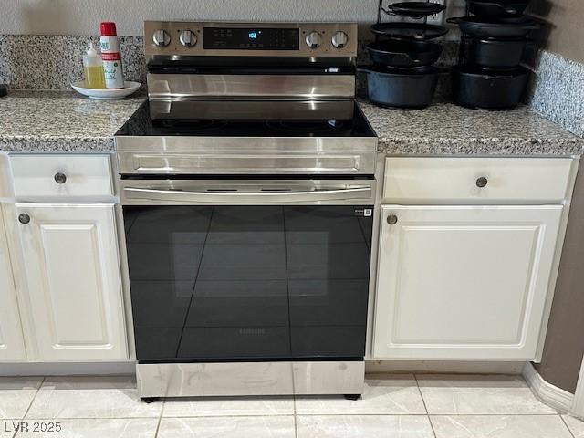 kitchen with white cabinets, light tile patterned floors, light stone counters, and stainless steel electric stove