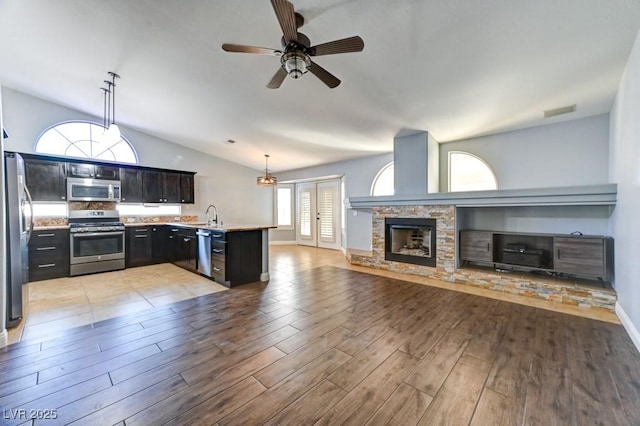 kitchen featuring kitchen peninsula, hanging light fixtures, stainless steel appliances, and a stone fireplace