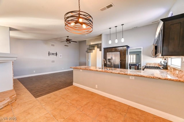 kitchen featuring dark brown cabinets, stove, light stone countertops, and stainless steel refrigerator with ice dispenser