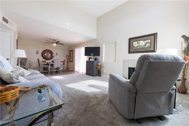 carpeted living area with a ceiling fan, baseboards, visible vents, and a tiled fireplace