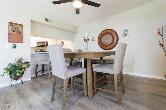 dining space with a ceiling fan, visible vents, baseboards, and wood finished floors