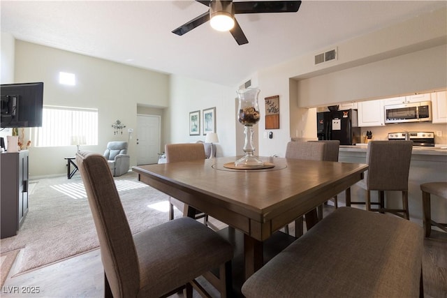 dining room with lofted ceiling, light colored carpet, visible vents, and a ceiling fan