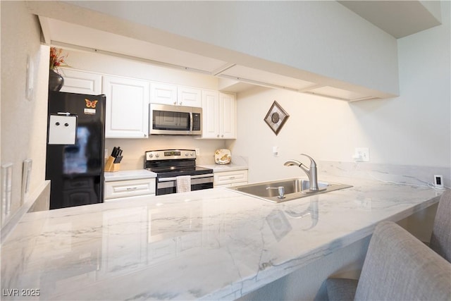 kitchen with light stone counters, a peninsula, a sink, white cabinetry, and appliances with stainless steel finishes