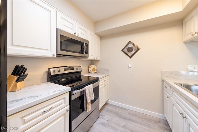 kitchen featuring baseboards, white cabinets, light stone countertops, stainless steel appliances, and light wood-type flooring