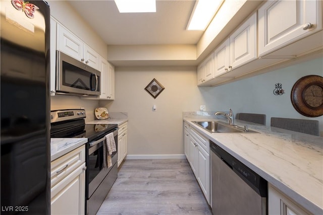 kitchen featuring a sink, white cabinetry, baseboards, appliances with stainless steel finishes, and light wood finished floors