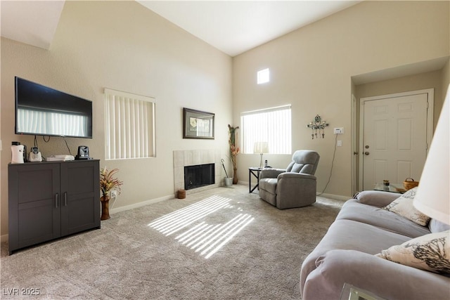 living area featuring light carpet, a high ceiling, baseboards, and a tiled fireplace