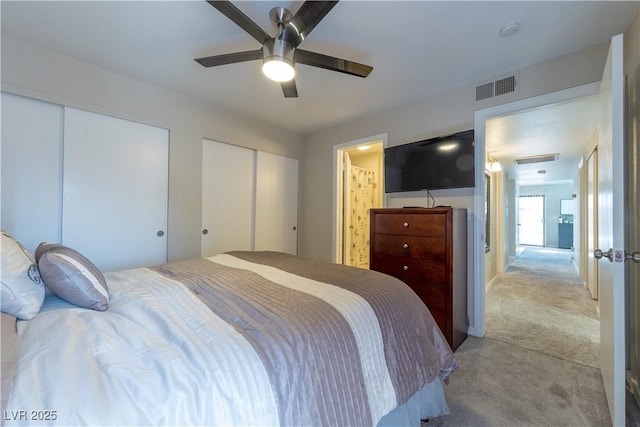 bedroom featuring light carpet, ceiling fan, visible vents, and multiple closets