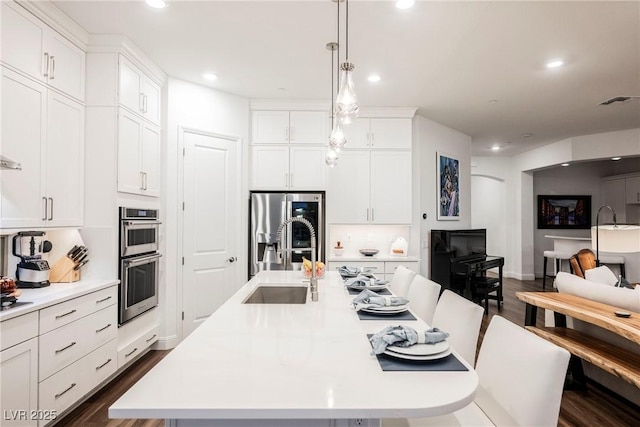 kitchen featuring dark wood-type flooring, hanging light fixtures, an island with sink, white cabinets, and appliances with stainless steel finishes