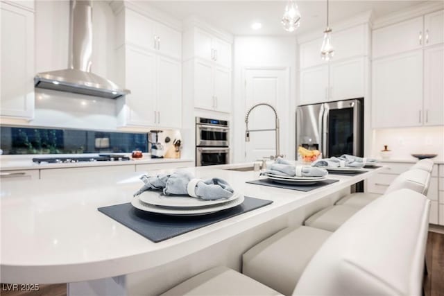 kitchen with wall chimney range hood, a breakfast bar, hanging light fixtures, and appliances with stainless steel finishes