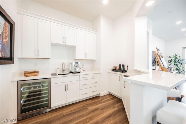 kitchen featuring beverage cooler, kitchen peninsula, dark hardwood / wood-style flooring, sink, and white cabinetry