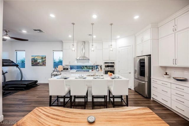 kitchen featuring appliances with stainless steel finishes, an island with sink, white cabinets, and wall chimney exhaust hood