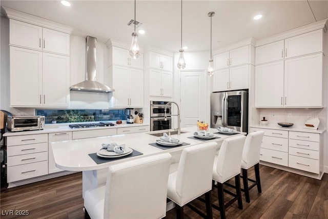 kitchen featuring appliances with stainless steel finishes, a kitchen island with sink, a breakfast bar area, and wall chimney exhaust hood