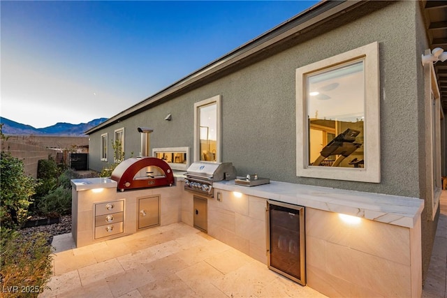 patio terrace at dusk featuring beverage cooler, area for grilling, and a mountain view