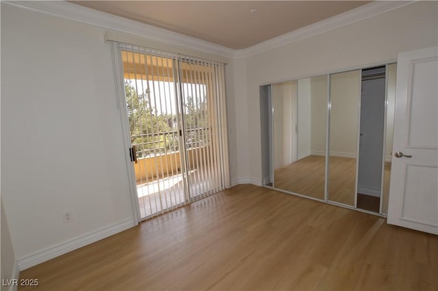 unfurnished bedroom featuring a closet, ornamental molding, wood finished floors, access to outside, and baseboards