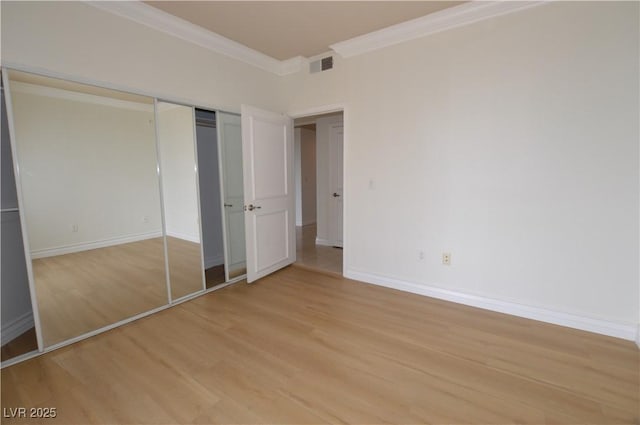 unfurnished bedroom featuring light wood finished floors, baseboards, visible vents, ornamental molding, and a closet