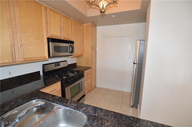 kitchen with light tile patterned floors, stainless steel appliances, a sink, dark stone counters, and light brown cabinetry