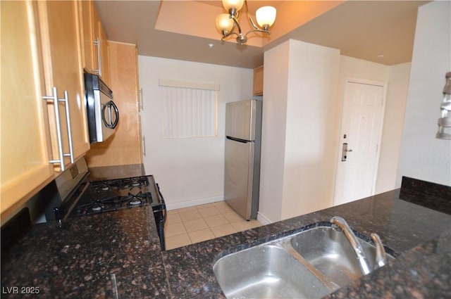 kitchen with light tile patterned floors, stainless steel appliances, an inviting chandelier, a sink, and dark stone countertops